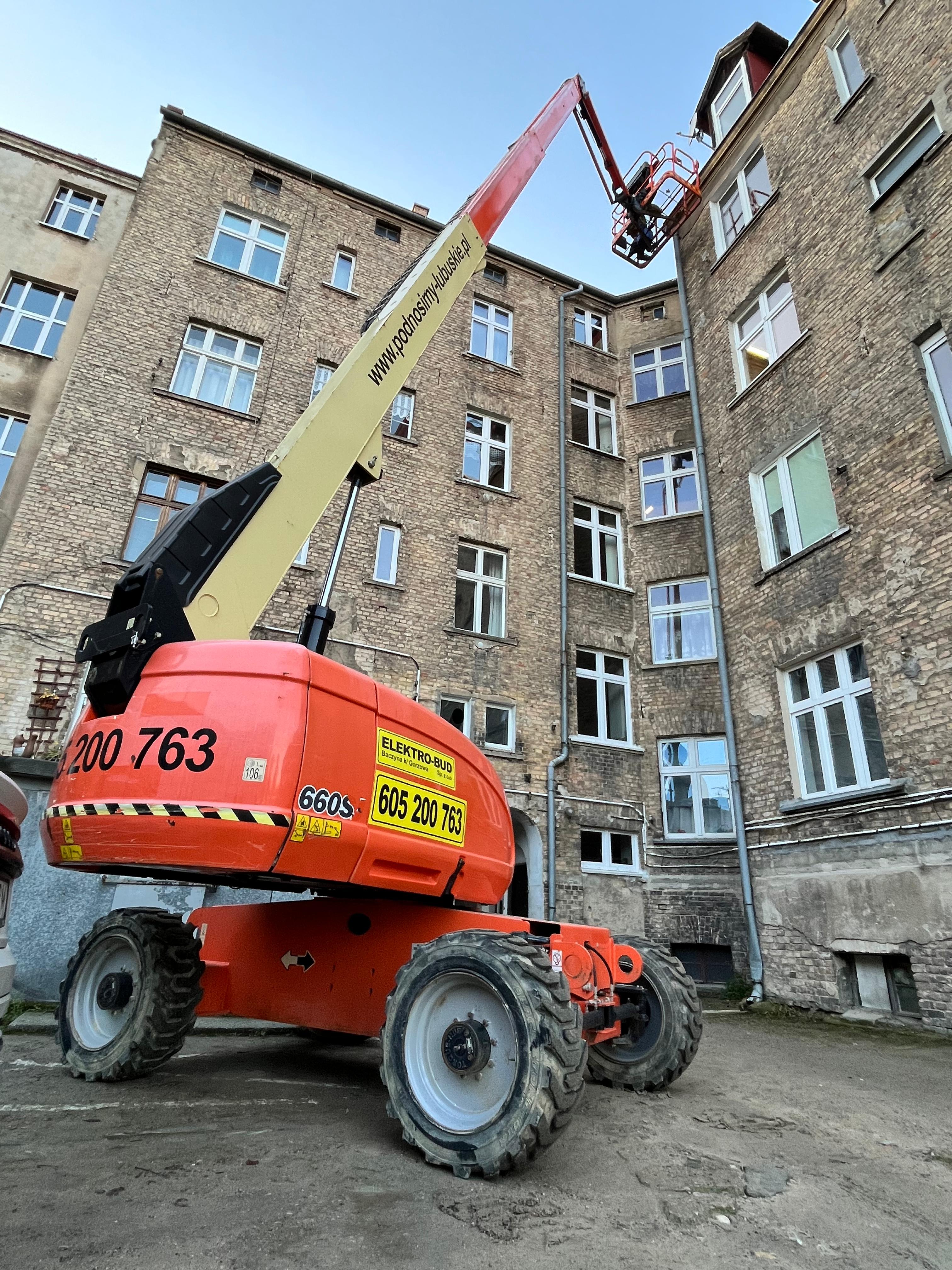 Podnośnik koszowy Elektro-Bud podczas prac na wysokości przy elewacji kamienicy, z wysięgnikiem teleskopowym sięgającym dachu budynku
